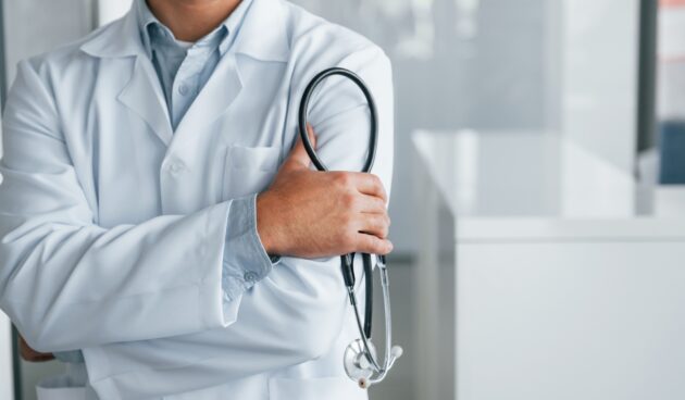 Stethoscope in hands. Professional medic in white coat is in the clinic